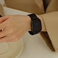 A close-up of a person's wrist wearing a black smartwatch with a black mesh band, styled with a beige trench coat sleeve, Obroi