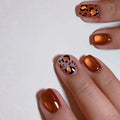 Hand with bronze nail polish and leopard print design on a white background, Obroi