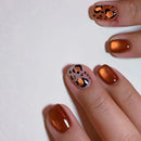 Hand with bronze nail polish and leopard print design on a white background, Obroi