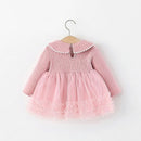 A pink toddler girl's dress with a ribbed knit long-sleeve bodice, a ruffled Peter Pan collar, and a layered tulle skirt, hanging on a wooden hanger against a plain white background, Obroi