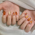 Close-up of hands with orange and gold glittery nail designs on a white background, Obroi