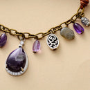 Bracelet with various charms including purple teardrop pendants and a textured metal circle on a beige background, Obroi