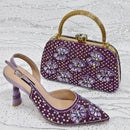 A purple embellished slingback high heel shoe and a matching purple handbag with a gold handle, both decorated with floral beadwork and rhinestones, displayed on a sparkly white background, Obroi