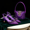 Purple pointed-toe slingback heels with rhinestone embellishments displayed beside a matching purple rhinestone handbag on a dark green velvet draped table against a black background, Obroi