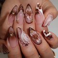 Nails with floral and butterfly designs in brown, white, and gold on a neutral background, Obroi