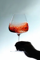 Hand holding a glass of red wine against a light background, Obroi