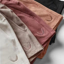Four pairs of folded shorts in different muted colors—cream, taupe, dusty rose, peach, and black—arranged diagonally. Each pair has a small embroidered leaf-like logo near the lower edge, Obroi