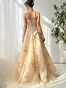 Woman wearing a beige evening gown with floral embroidery in a bright room, Obroi
