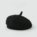 A black textured bouclé beret hat with a short top handle, photographed on a clean light gray background, Obroi