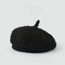 A black textured bouclé beret hat with a short top handle, photographed on a clean light gray background, Obroi