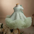 A baby girl's formal dress displayed on a dress form mannequin. The dress is a pale mint green with white floral lace applique on the bodice and a layered, ruffled tulle skirt, Obroi