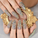 Hand with ornate gemstone nail art in front of a decorative gold mirror, Obroi
