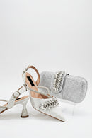 White high-heeled shoes with decorative embellishments and a matching silver clutch on a white background, Obroi