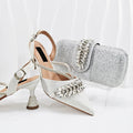 White high-heeled shoes with decorative embellishments and a matching silver clutch on a white background, Obroi