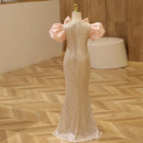 Gold evening gown on a mannequin with pink ribbons against a wooden floor background, Obroi