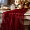 Red sheer fabric with beading on a table with blurred floral arrangement in the background, Obroi