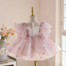 A pink tulle dress with floral embroidery and ruffled sleeves displayed on a mannequin in a softly lit indoor setting, Obroi