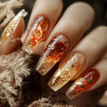 Nails with a red and gold glitter design held against a textured surface, Obroi