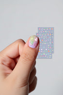 Nail art with colorful stickers on a light gray background, Obroi