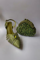 Green high-heeled shoe with embellishments and a matching green handbag on a light gray background, Obroi