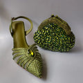 Green high-heeled shoe with embellishments and a matching green handbag on a light gray background, Obroi