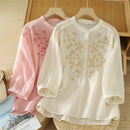 Two embroidered shirts, one pink and one white, on hangers against a wooden background, Obroi