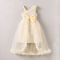 A sleeveless cream-colored baby dress with a textured knit bodice, a large matching bow at the waist, and a layered tulle skirt with ruffled trim, shown against a plain light gray background, Obroi