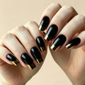 A close-up of hands with glossy black coffin-shaped nails featuring a metallic gold French tip design, set against a soft beige background, Obroi