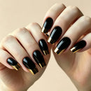 A close-up of hands with glossy black coffin-shaped nails featuring a metallic gold French tip design, set against a soft beige background, Obroi