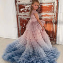 Young girl in a pink and blue ruffled dress standing in front of a rustic wooden door, Obroi