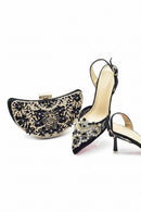 A pair of black velvet high-heeled slingback sandals with ornate gold and crystal embellishments, shown alongside a matching black and gold clutch purse on a white background. The brand name 'Obroi' is printed in black text in the top-left corner.