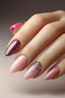 A close-up of a hand with long almond-shaped nails styled in a pink manicure, featuring two glittery rose-pink accent nails and a pale pink nail with fine silver glitter, Obroi