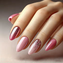 A close-up of a hand with long almond-shaped nails styled in a pink manicure, featuring two glittery rose-pink accent nails and a pale pink nail with fine silver glitter, Obroi