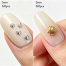 Two close-up nail sample photos side by side showing shell-shaped nail decorations applied on fingernails. The left photo shows four small silver shell charms labeled 3mm, 500pcs; the right photo shows one larger gold shell charm labeled 5mm, 500pcs, Obroi