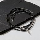 Black beaded bracelets with silver accents on a dark stone surface, Obroi
