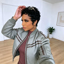 A woman takes a mirror selfie wearing a light sage green bomber jacket with brown stripes, a ribbed mauve-brown top, and gold hoop earrings. She has sunglasses on her head and is in a bright room with light wood floors and white walls, Obroi