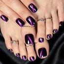 Close-up of feet with manicured toenails in a glossy metallic deep purple shade, styled with several delicate rings against a black fabric background, Obroi