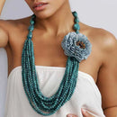 Turquoise beaded necklace with a large floral pendant on a model against a white background, Obroi