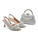 Silver high-heeled shoes and matching handbag with floral embellishments on a white background, Obroi