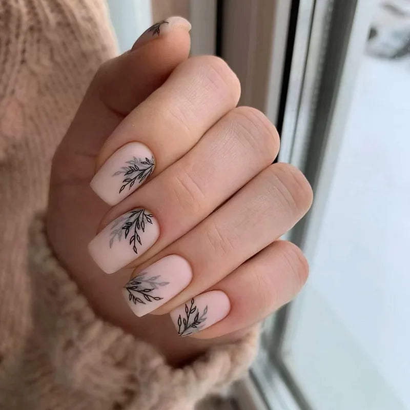 Nails with black leaf designs on a neutral background