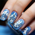Nails with blue nail polish and white floral designs on a dark background, Obroi