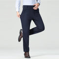 Person wearing navy blue dress pants with a white shirt and brown shoes on a light gray background, Obroi