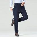 Person wearing navy blue dress pants with a white shirt and brown shoes on a light gray background, Obroi