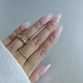 Hand with pink nail art and a gold ring on a light gray background, Obroi