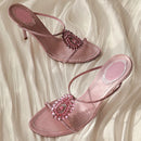Pink high-heeled sandals with embellishments on a soft fabric background, Obroi