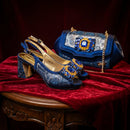 Blue high-heeled shoes with gold accents and a matching blue handbag on a red fabric background, Obroi