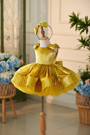 Yellow children's dress on a mannequin with a blurred floral and indoor plant background, Obroi