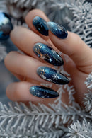 Nails with dark blue glittery design held against a blurred background, Obroi