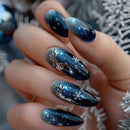 Nails with dark blue glittery design held against a blurred background, Obroi