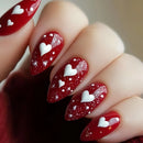 Red nail polish with white heart designs on a neutral background, Obroi